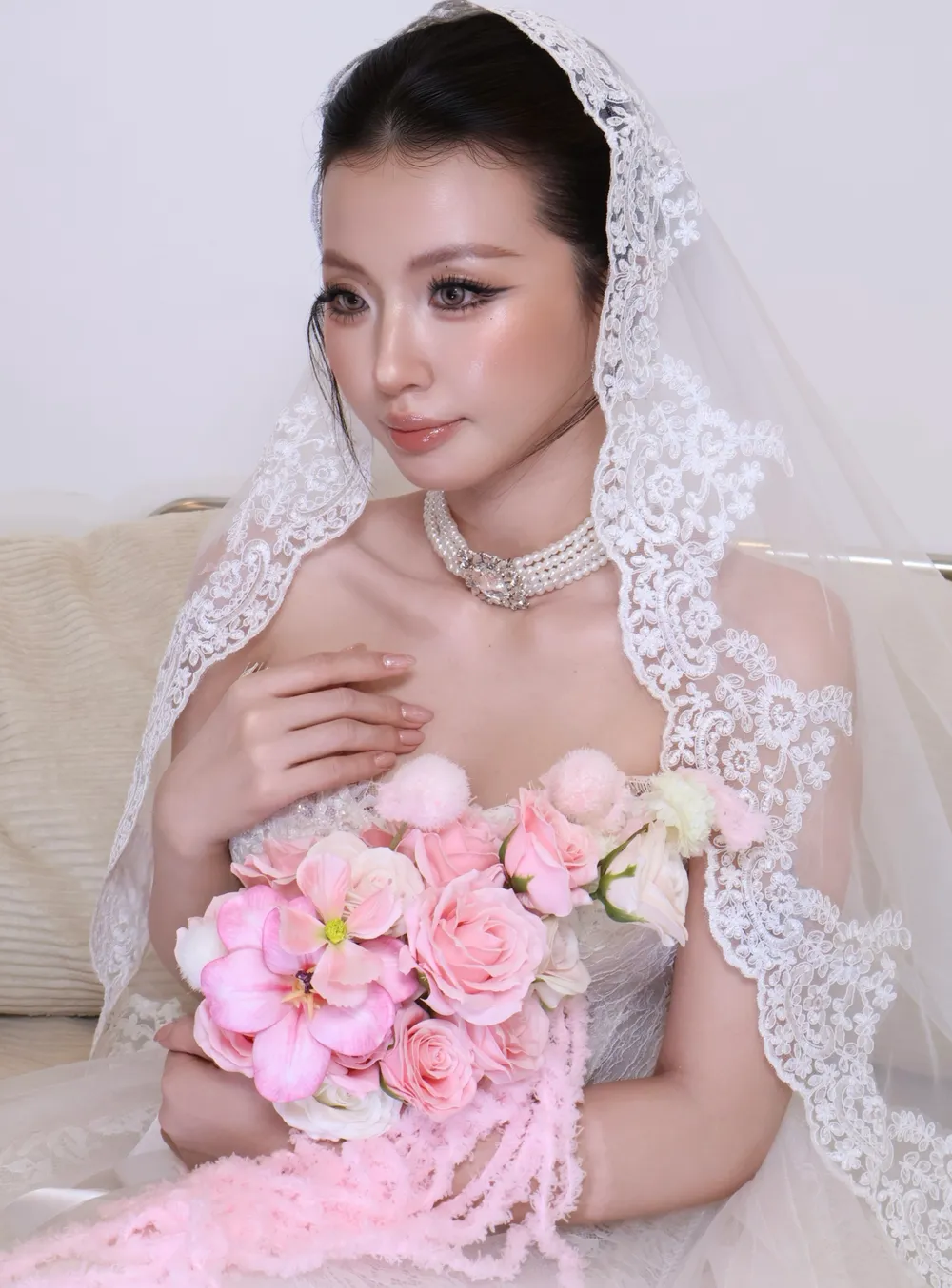 Cô dâu trong váy cưới ren, tay chạm nhẹ ngực áo, voan ren buông dài xuống vai