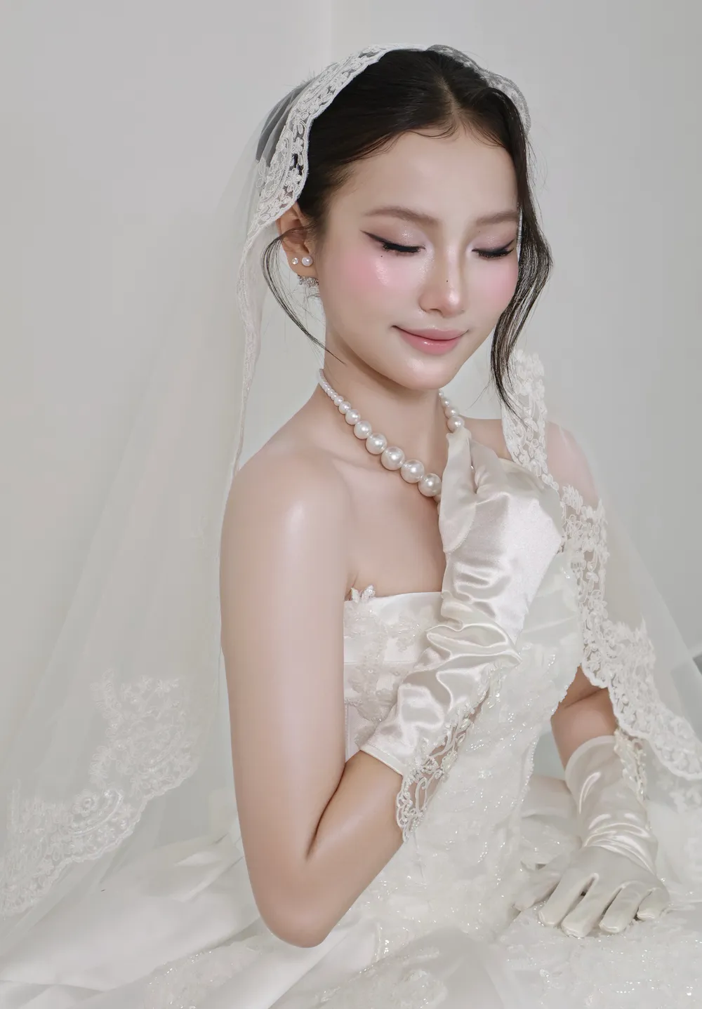 Cô dâu nhắm mắt cười nhẹ, má ửng hồng tự nhiên, chuỗi ngọc trai và găng lụa