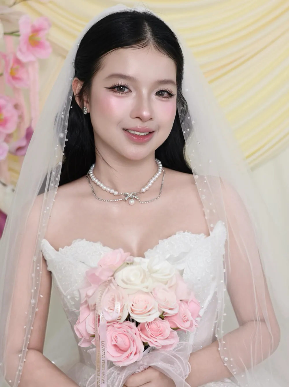 Cô dâu trang điểm ngọt ngào, đội voan tulle đính ngọc trai, cầm bó hoa hồng phấn